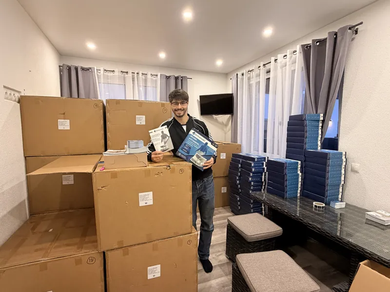 Alex steht zwischen Kartons und hält eine Orthamedic-Verpackung und die Gebrauchsanweisung