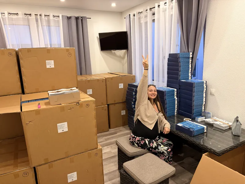 Valeria sitzt zwischen gestapelten Orthamedic-Verpackungen und zeigt ein Peace-Zeichen